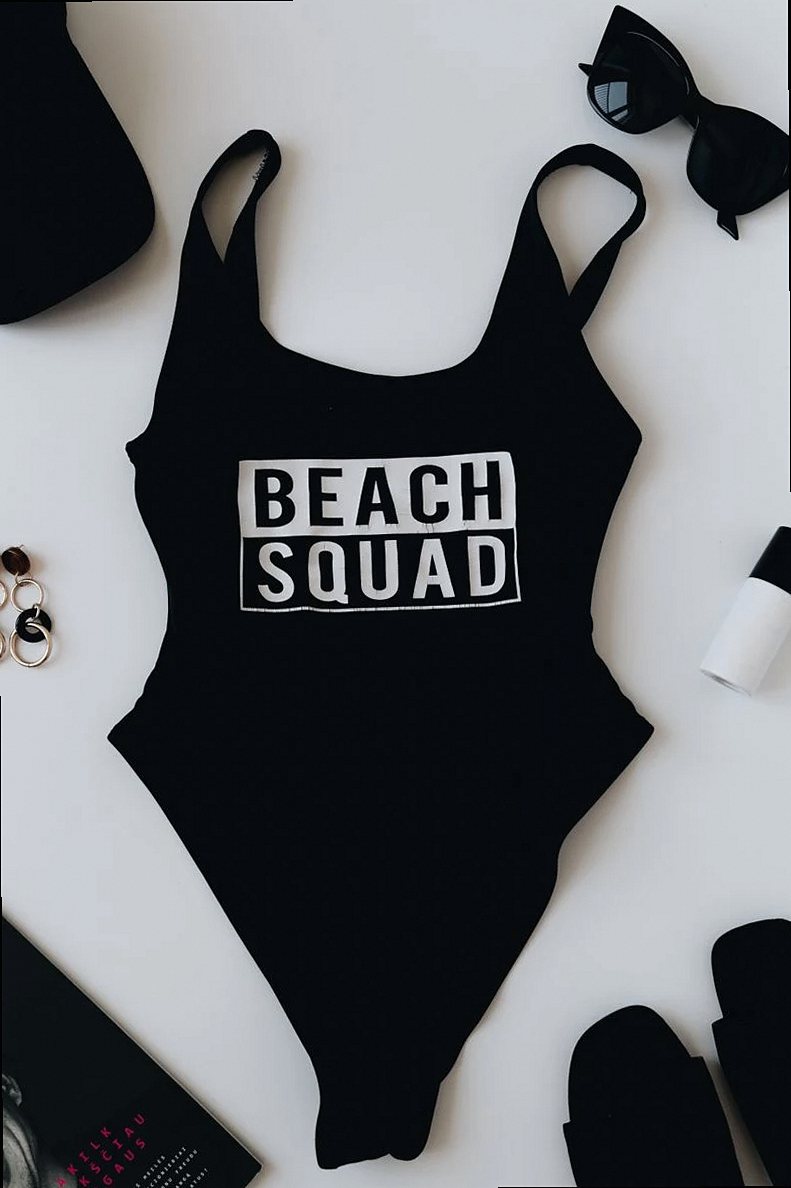 Top view of swimsuit with Beach Squad inscription near magazine and black sandals with sunglasses and cap with pair of e